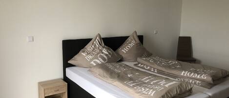 A bed with multiple pillows, a bedside table, and a small wooden nightstand.