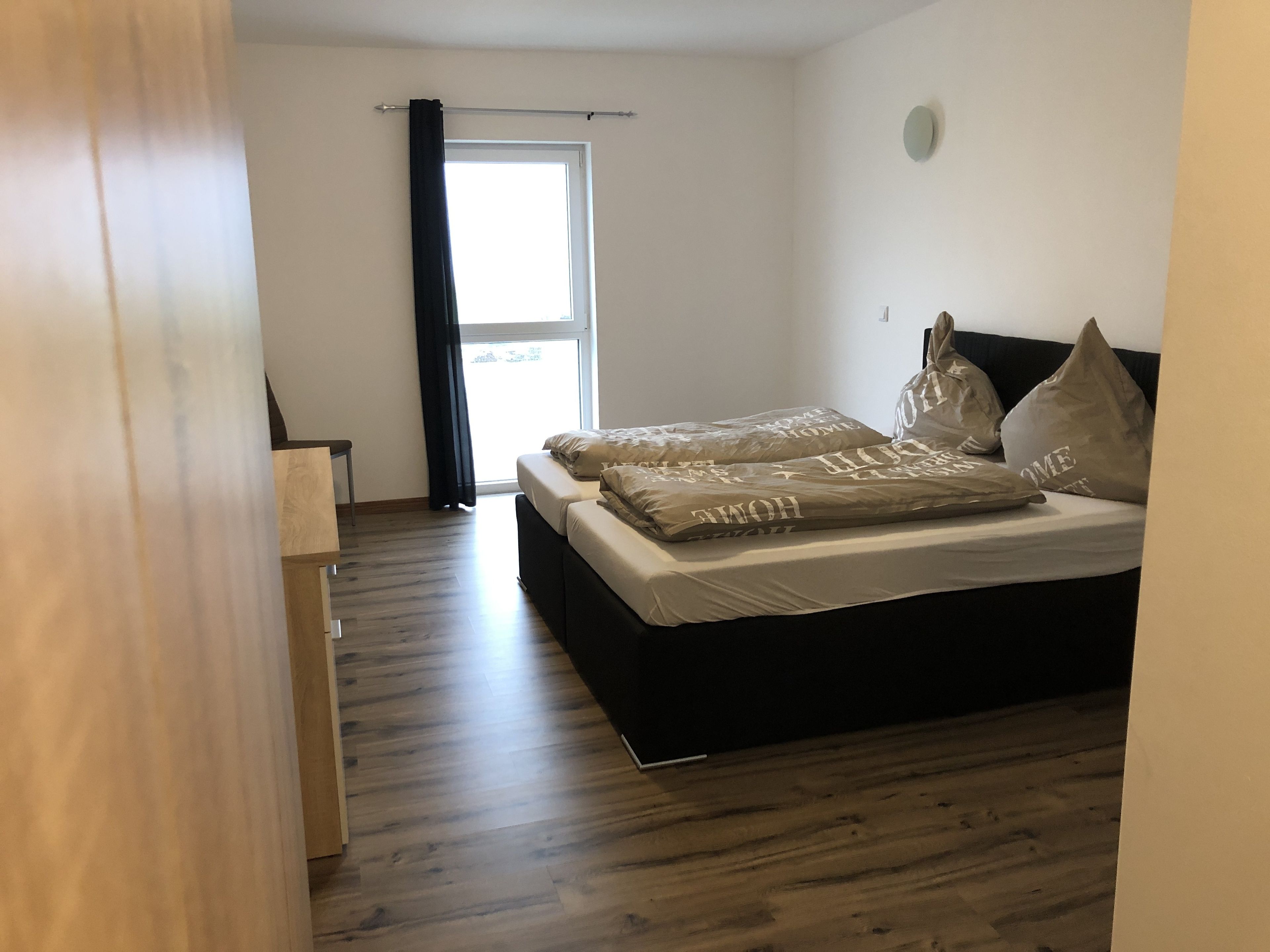 Una camera da letto con un letto, pavimento in legno, una finestra con tende e una porta.