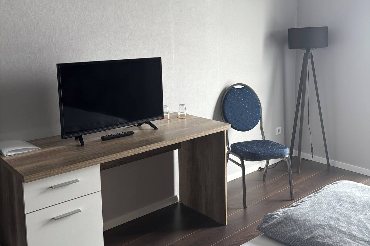 A modern bedroom with a wooden desk, a chair, a bed, and a floor lamp.