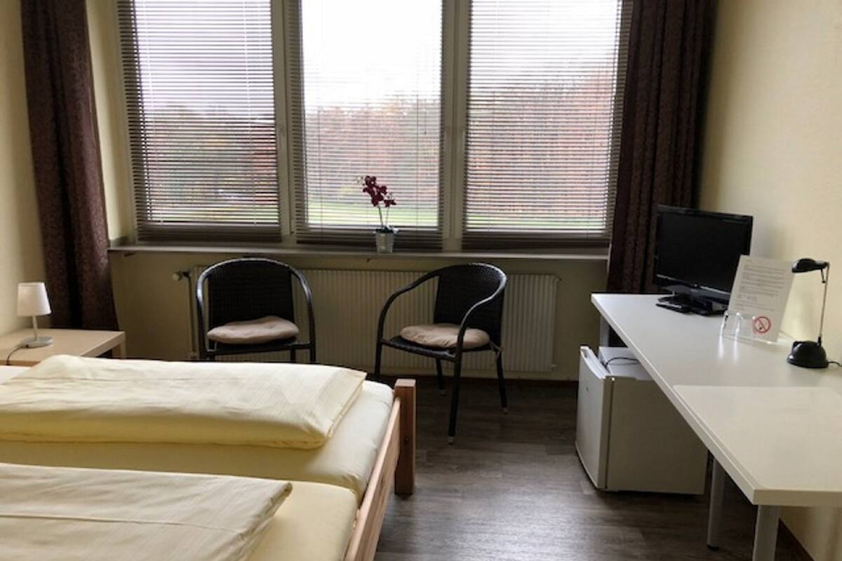 Una habitación de hotel con dos camas, un escritorio, una silla, un televisor y un radiador.