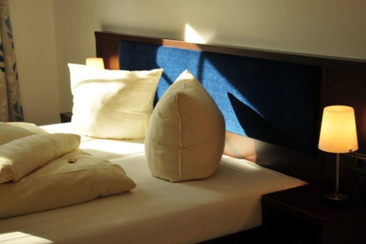 A hotel room with a bed, pillows, a nightstand, and a lamp.