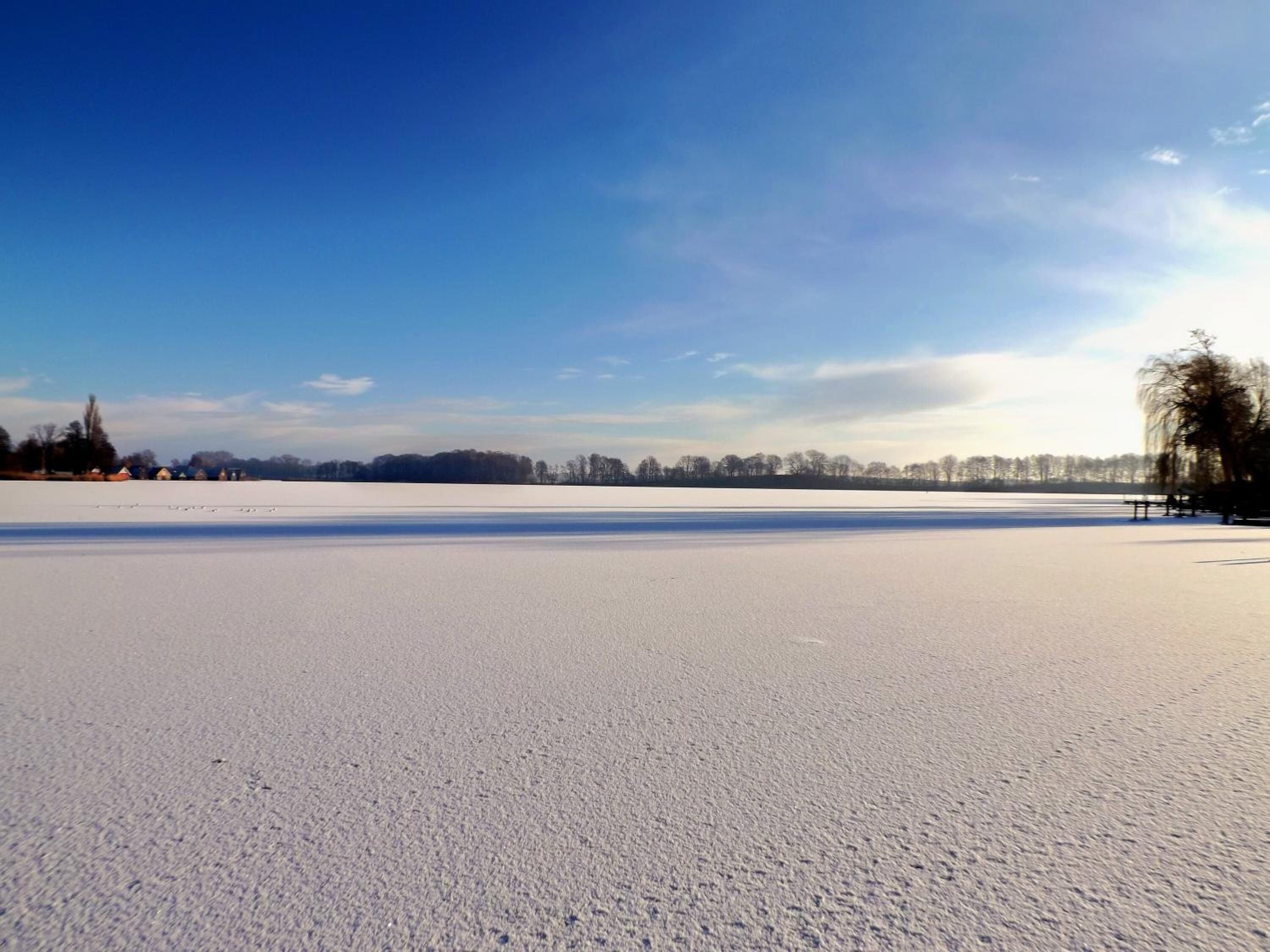 A vast, open snowy field with a clear blue sky.
