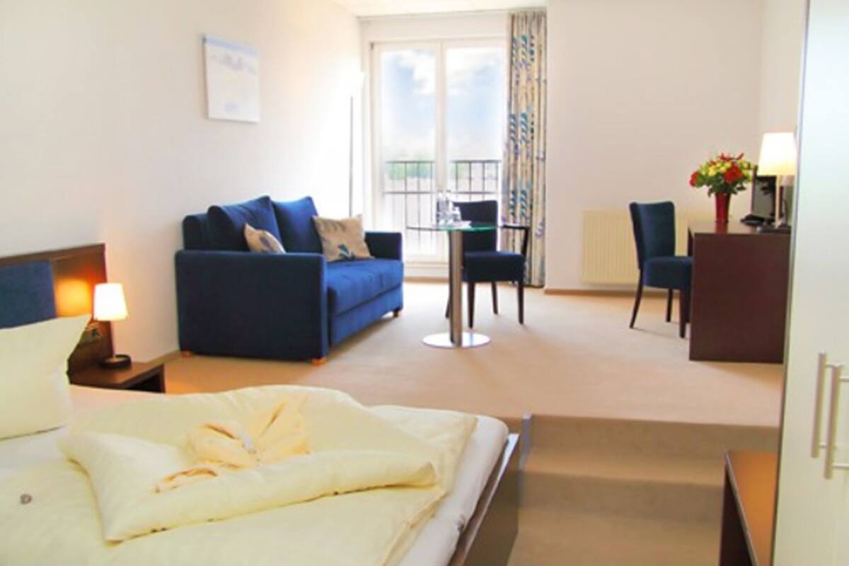 A hotel room with a bed, a blue sofa, a small table, and a chair.
