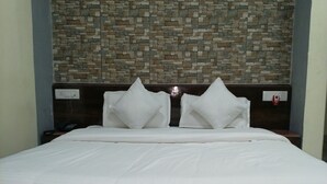 A bed with white bedding, a headboard with a stone-like pattern, and a dark-colored floor. - Tropical Suites (Phuntsholing)