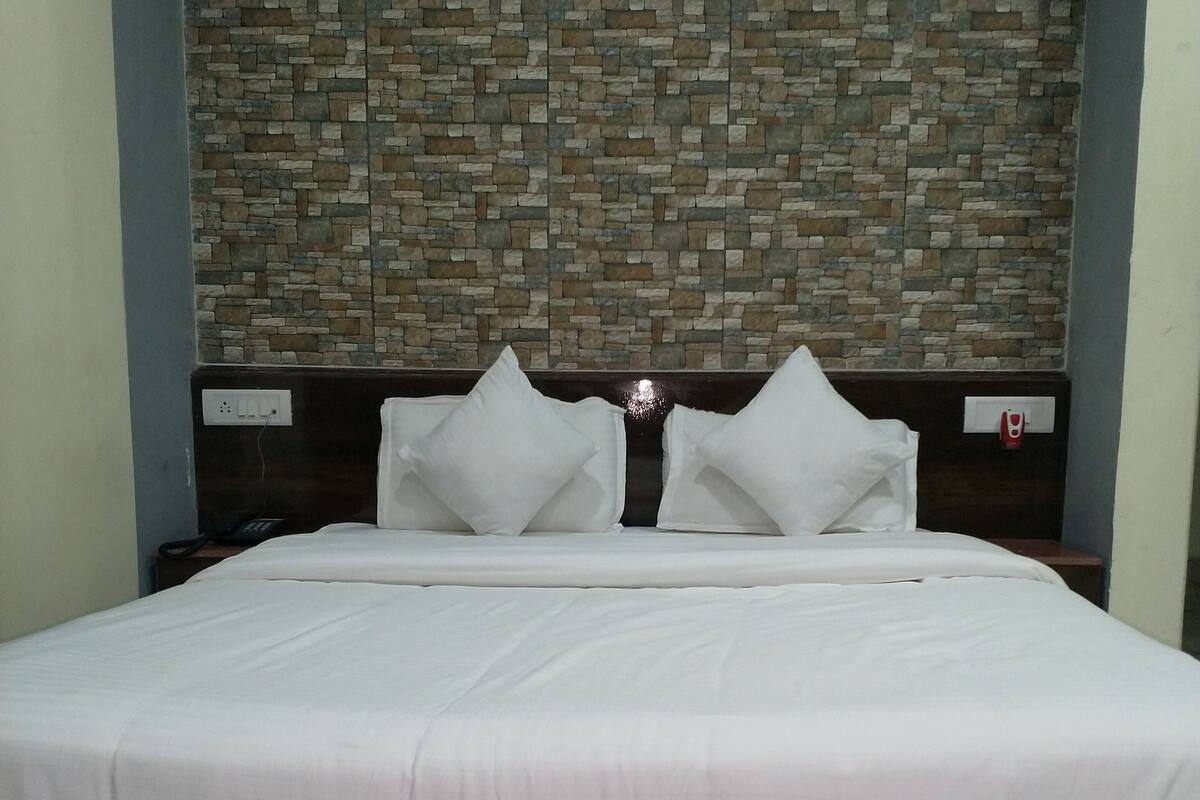 A bed with white bedding, a headboard with a stone-like pattern, and a dark-colored floor.