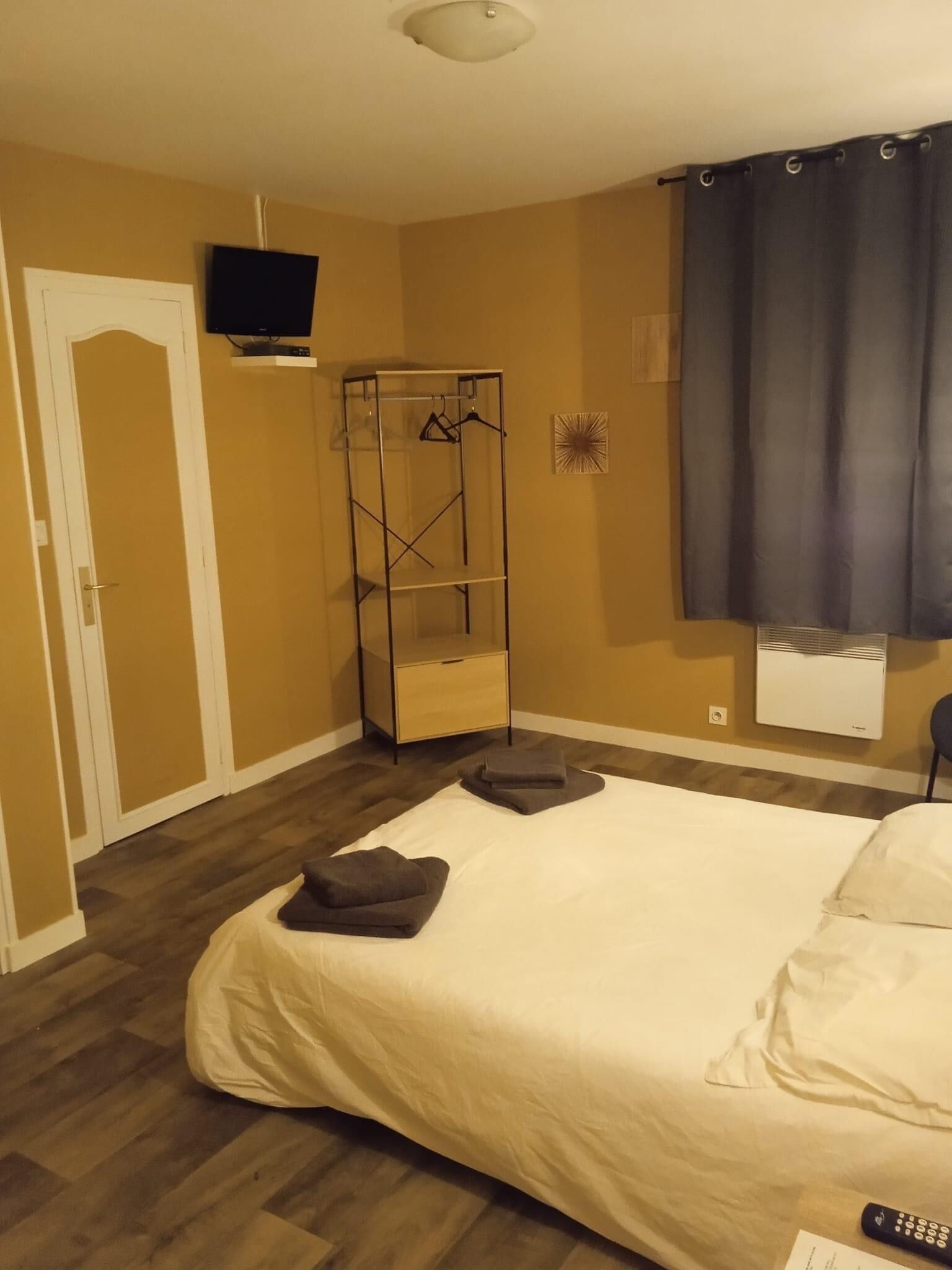 A bedroom with a bed, a TV mounted on the wall, a wardrobe, and a window with curtains.