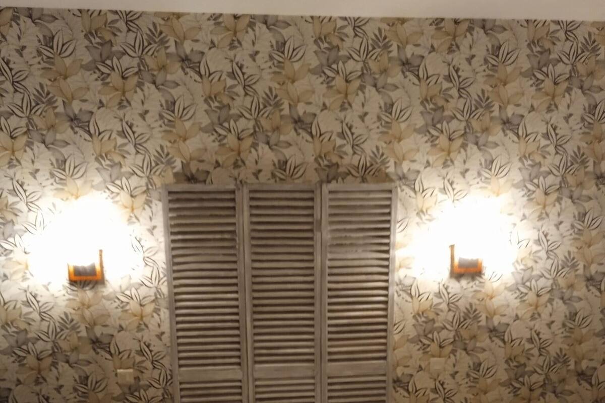 Un dormitorio con cama, dos almohadas, una mesita de noche y una pared con estampado de hojas.