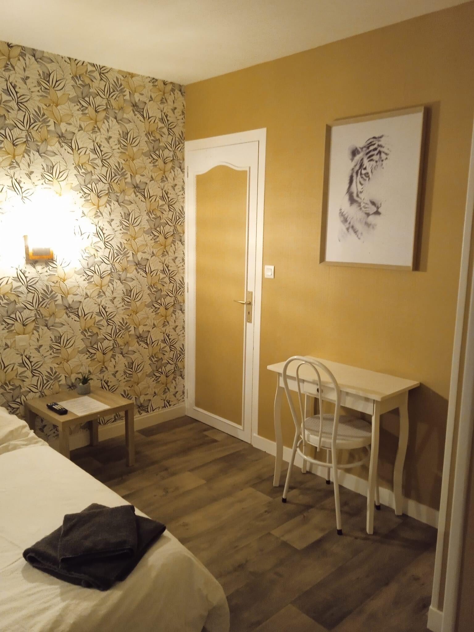 Una camera d'albergo con un letto, una scrivania, una sedia, un tavolino e un telecomando, più una parete con carta da parati a motivi floreali.