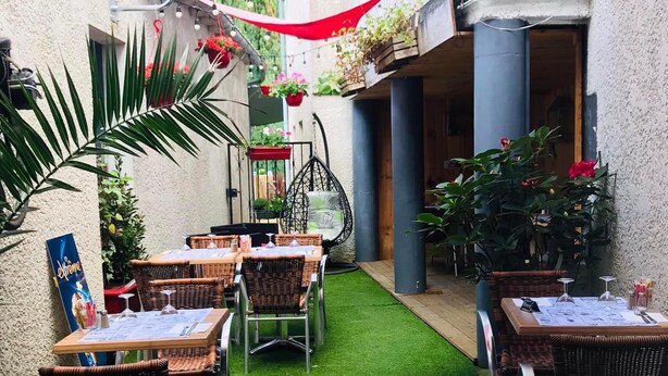 Eine Terrasse im Freien mit Korbstühlen und -stühlen, umgeben von Grünpflanzen und roten Markisen.