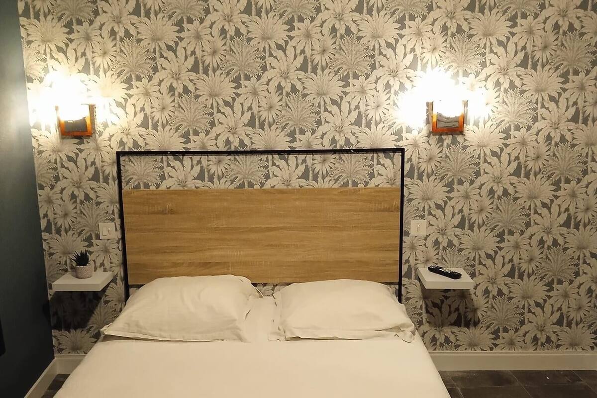 Una cama bien hecha con dos almohadas y dos toallas dobladas, cabecera de madera y un estampado floral en el papel tapiz.