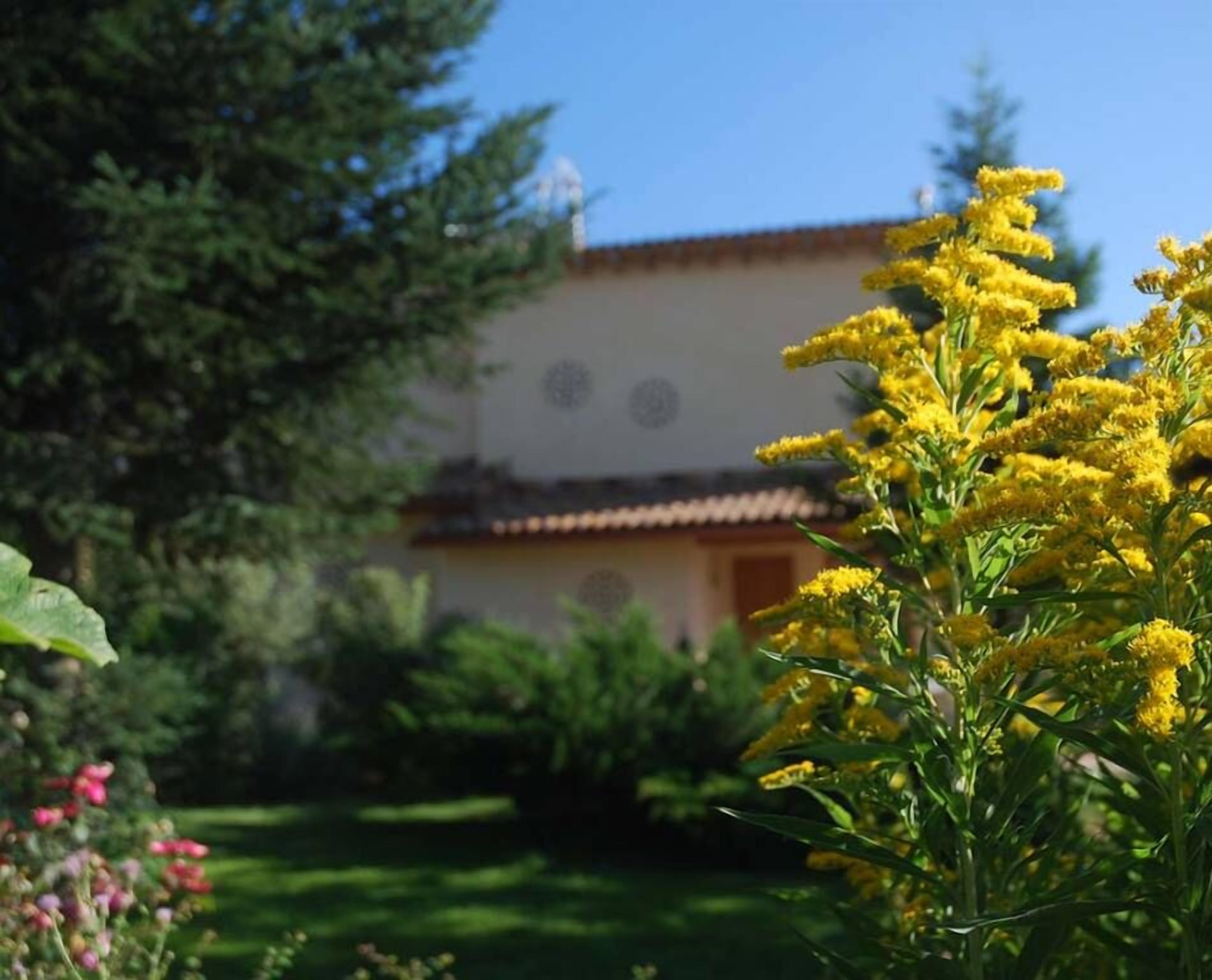 Un edificio con techo de tejas y un jardín con flores amarillas y arbustos verdes.