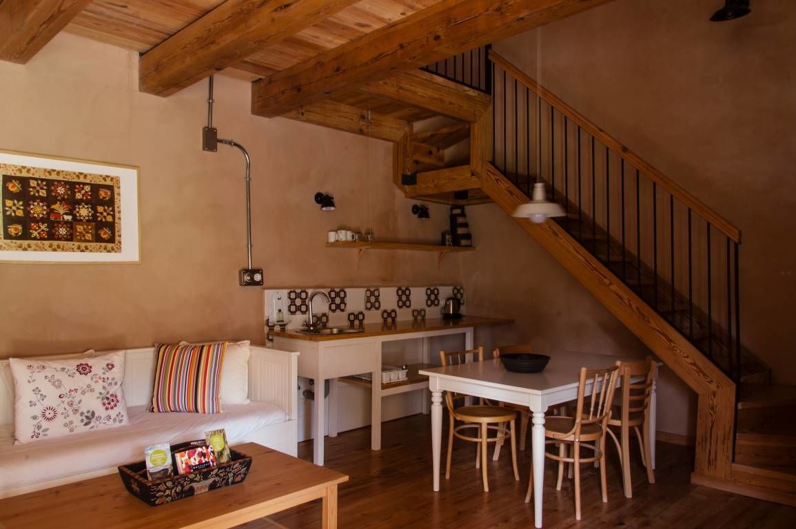 Una sala de estar acogedora con una escalera de madera, un comedor con una mesa y sillas blancas, y una cocina con salpicadero de azulejos.