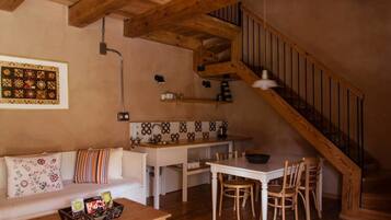 Una sala de estar acogedora con una escalera de madera, un comedor con una mesa y sillas blancas, y una cocina con salpicadero de azulejos.