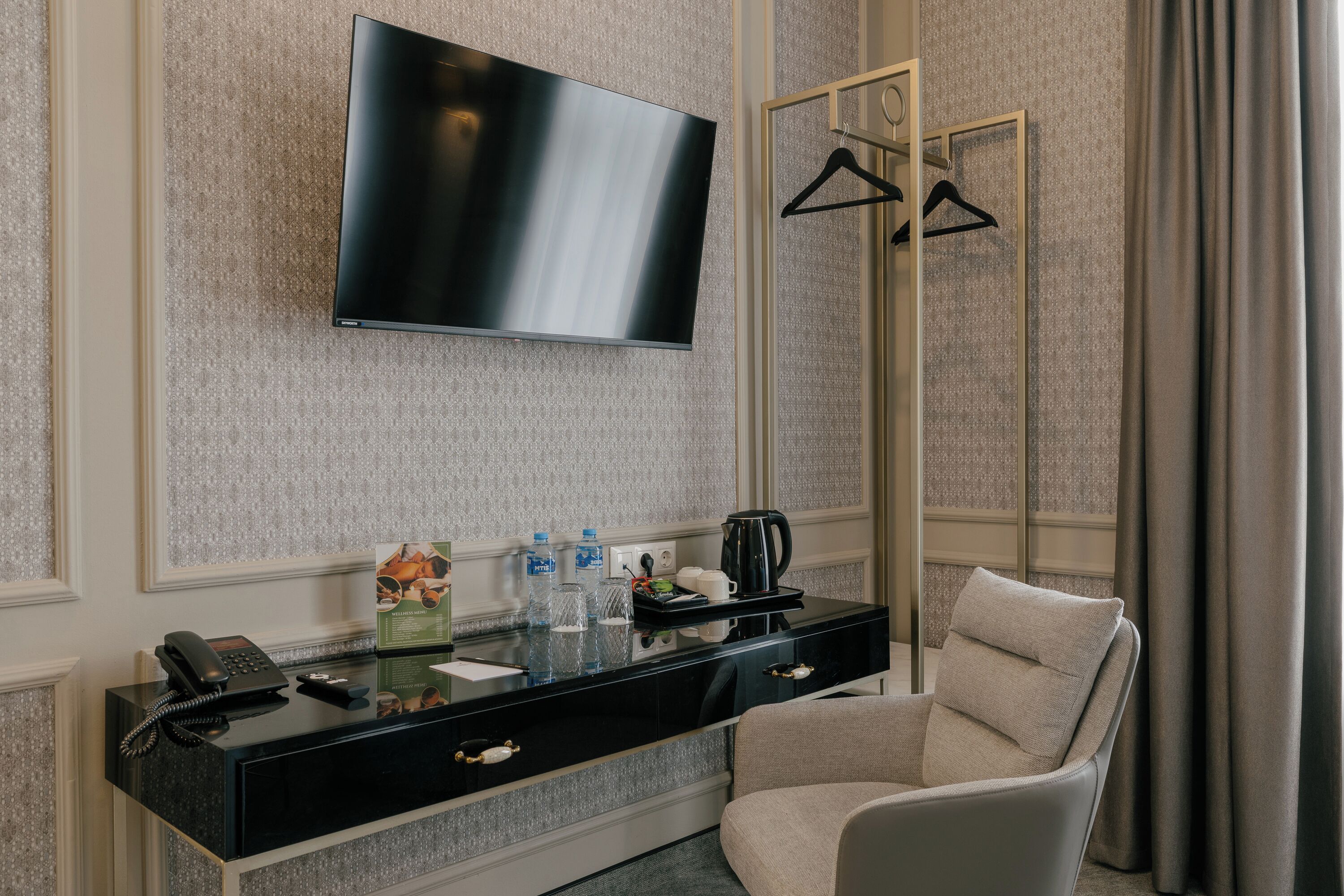 A hotel room with a flat-screen TV, a black console table with a phone, water bottles, and a coffee pot.