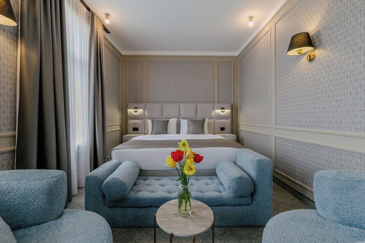 Habitació d'hotel amb un llit, dues butaques, una taula petita amb un ram de flors i aplics de paret.