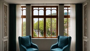 Una habitación con dos sillones azul verdosos, un ventanal con vista a un paisaje urbano y un papel tapiz estampado.