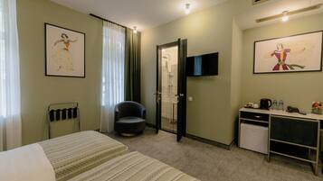 Habitación de hotel con cama, una silla, escritorio con computadora, ducha y dos cuadros en la pared.