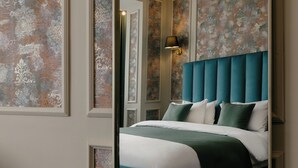 Una cama bien tendida con un cabecero color turquesa, una lámpara de pared y un papel tapiz estampado.