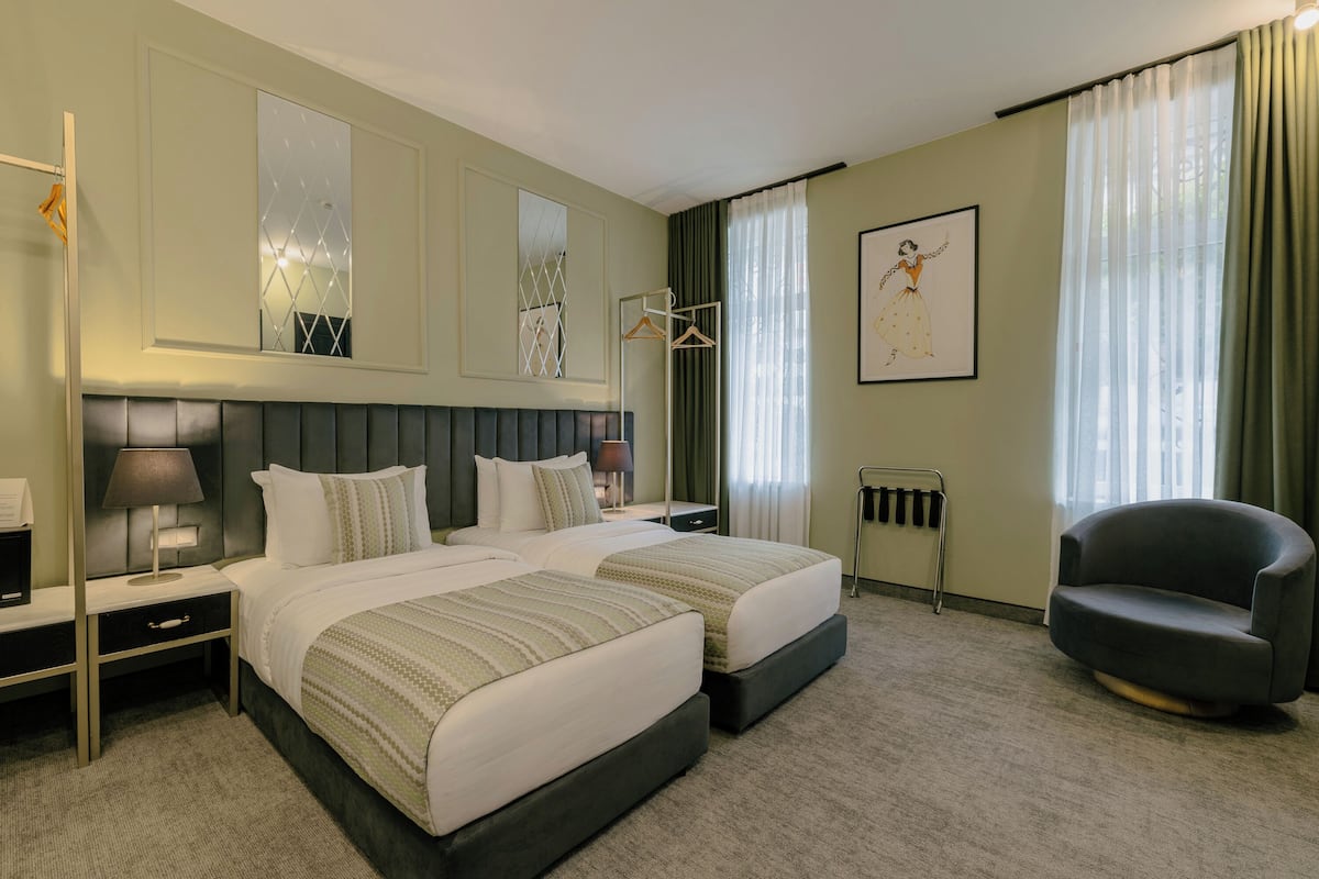 Habitació d'hotel amb dos llits, una cadira, un penjador i un quadre a la paret.