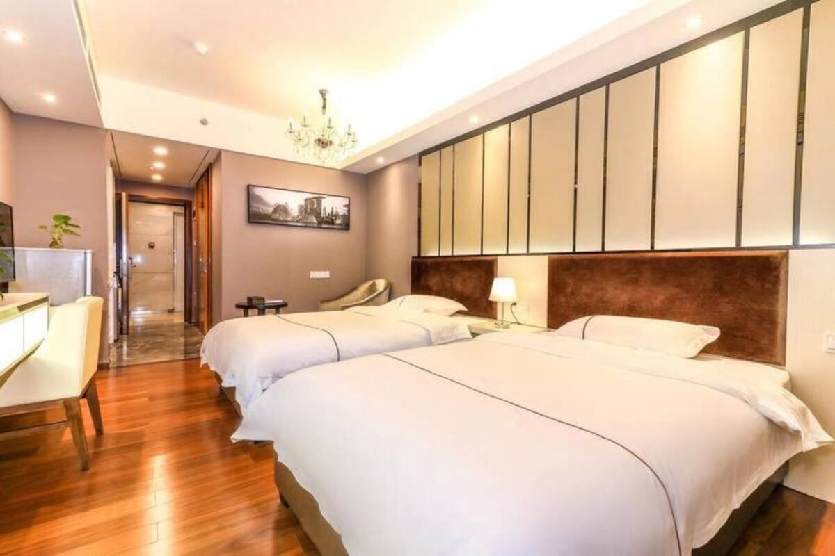 Ein Hotelzimmer mit zwei Betten, einem Schreibtisch, einem Stuhl, einer Chandelierleuchtre und einer Wand mit vertikalen Paneelen.
