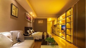 A modern hotel room with a sofa, a small table with a plant, a bed with a striped blanket, and a TV on a stand. - Atlantis International Holiday Apartment Hotel - Pazhou Guangzhou Tower (Guangzhou)