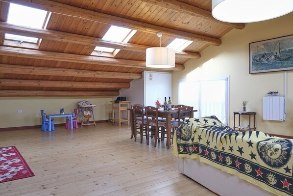 Une pièce mansardée spacieuse avec des poutres en bois, une table à manger, des chaises, un canapé et un tableau accroché au mur.
