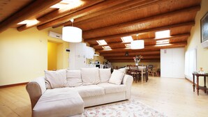 A spacious living area with a beige sofa, wooden ceiling beams, and a dining area in the background. - Agriturismo da Rosi - villa with pool, Casa Sofia (codevigo)