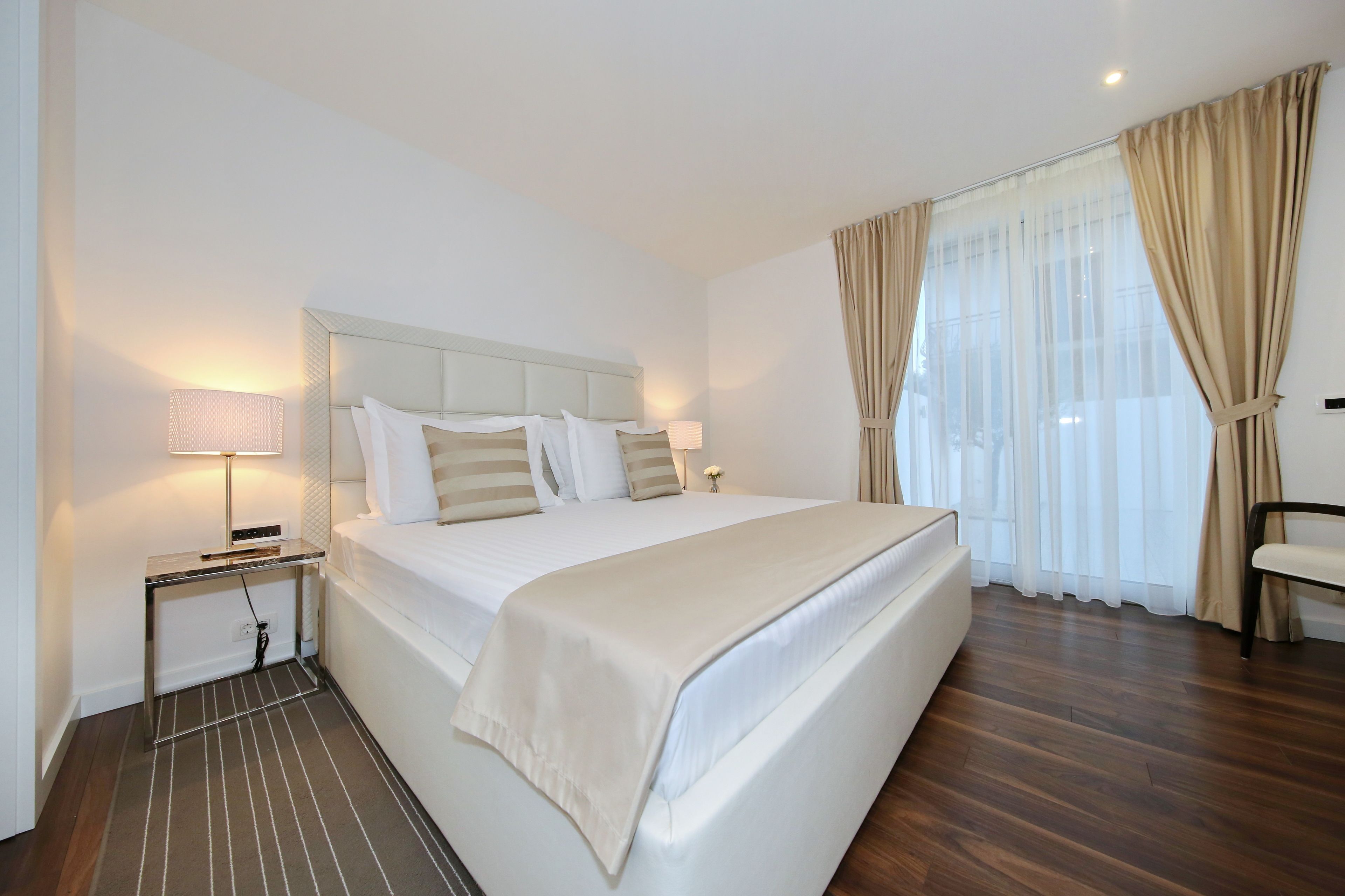 A neatly made bed with a headboard, a bedside table with a lamp, and a chair.