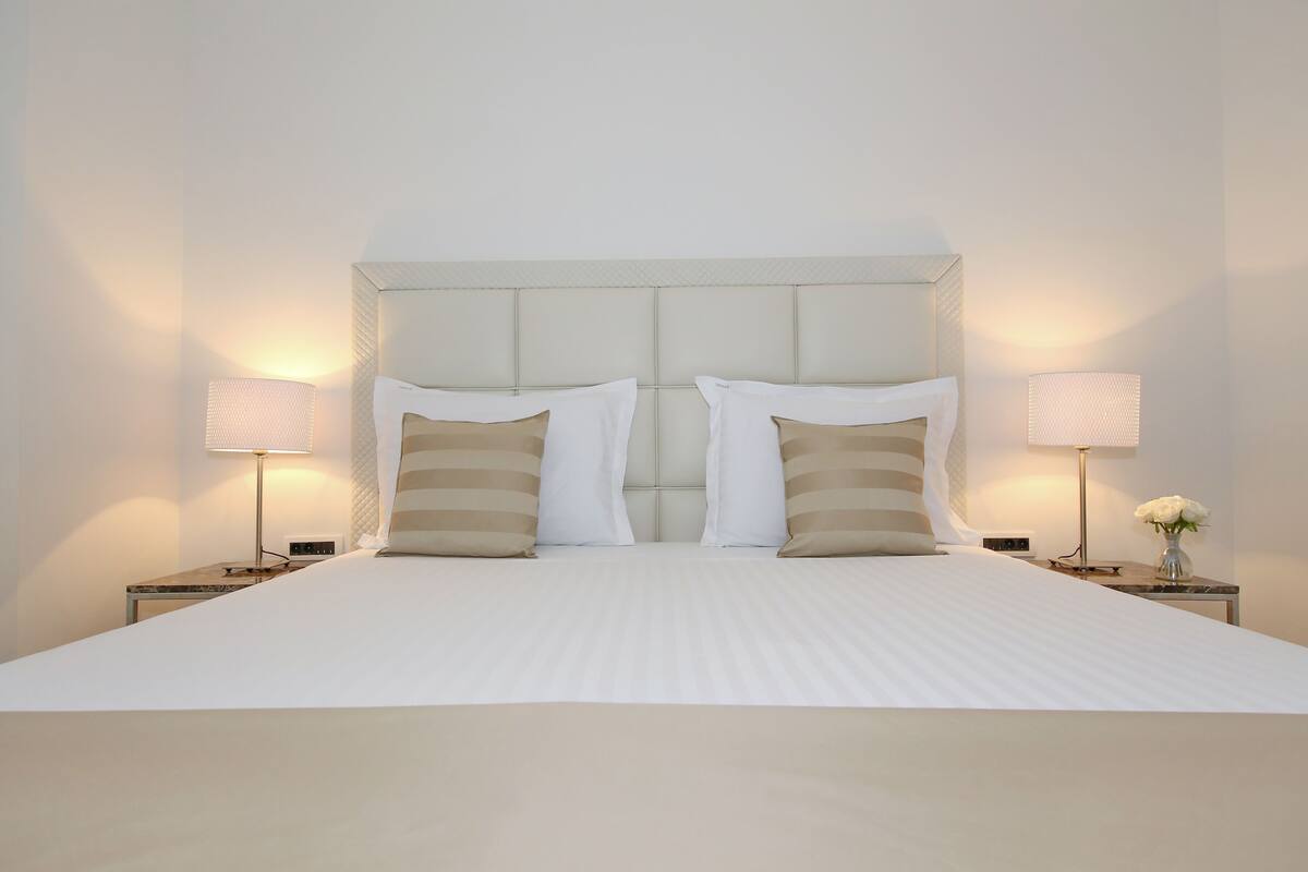 A neatly made bed with a white headboard and two bedside lamps.