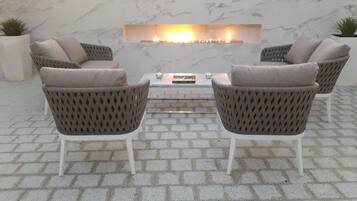 Un patio con dos sillas de mimbre, una mesita y una chimenea de ladrillo.