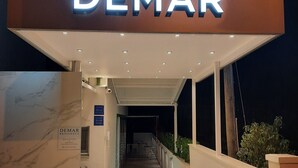 Una entrada de hotel moderna con un cartel 'DEMAR', un mostrador de recepción y una pared de mármol.