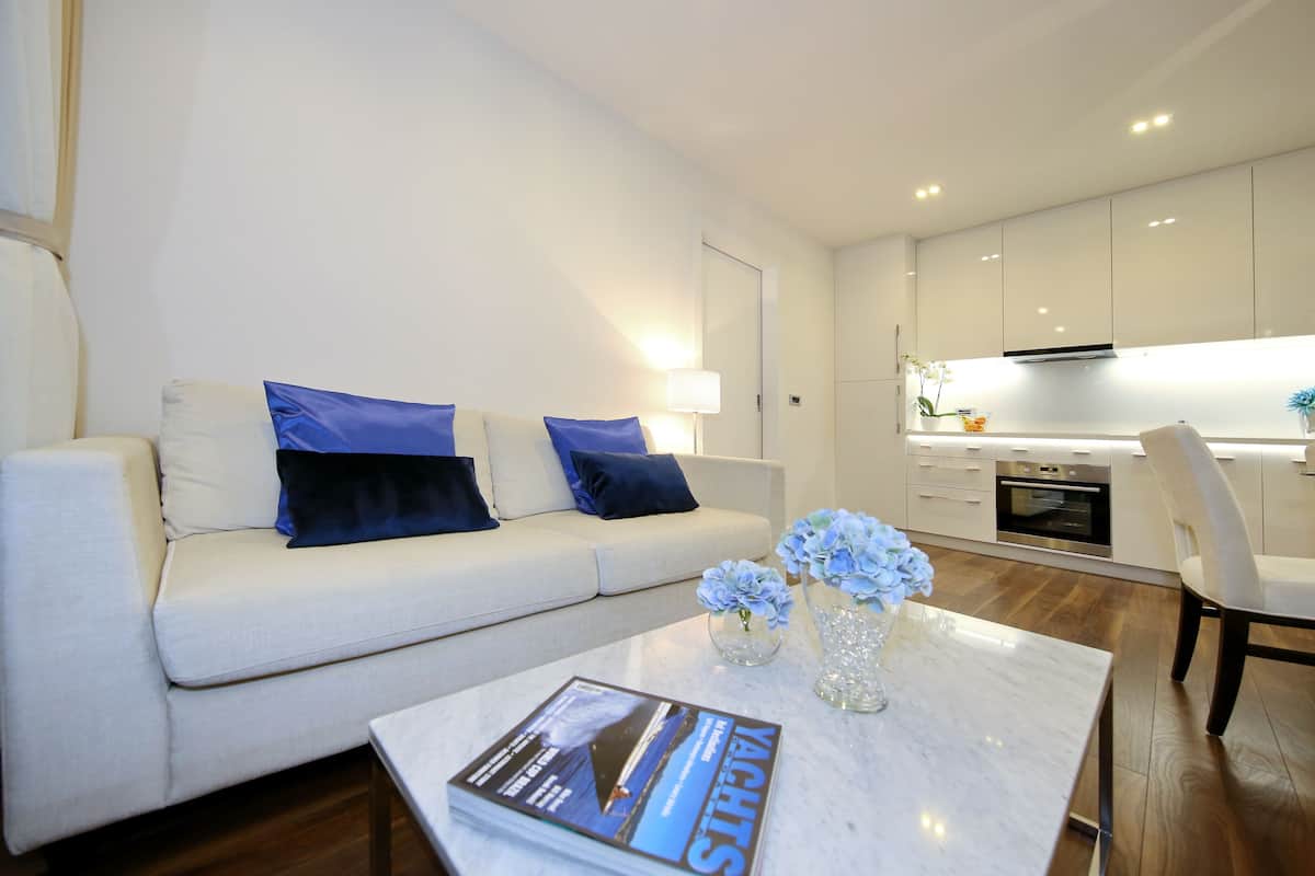 A modern living room with a sofa, a coffee table with a magazine, and a kitchen in the background.