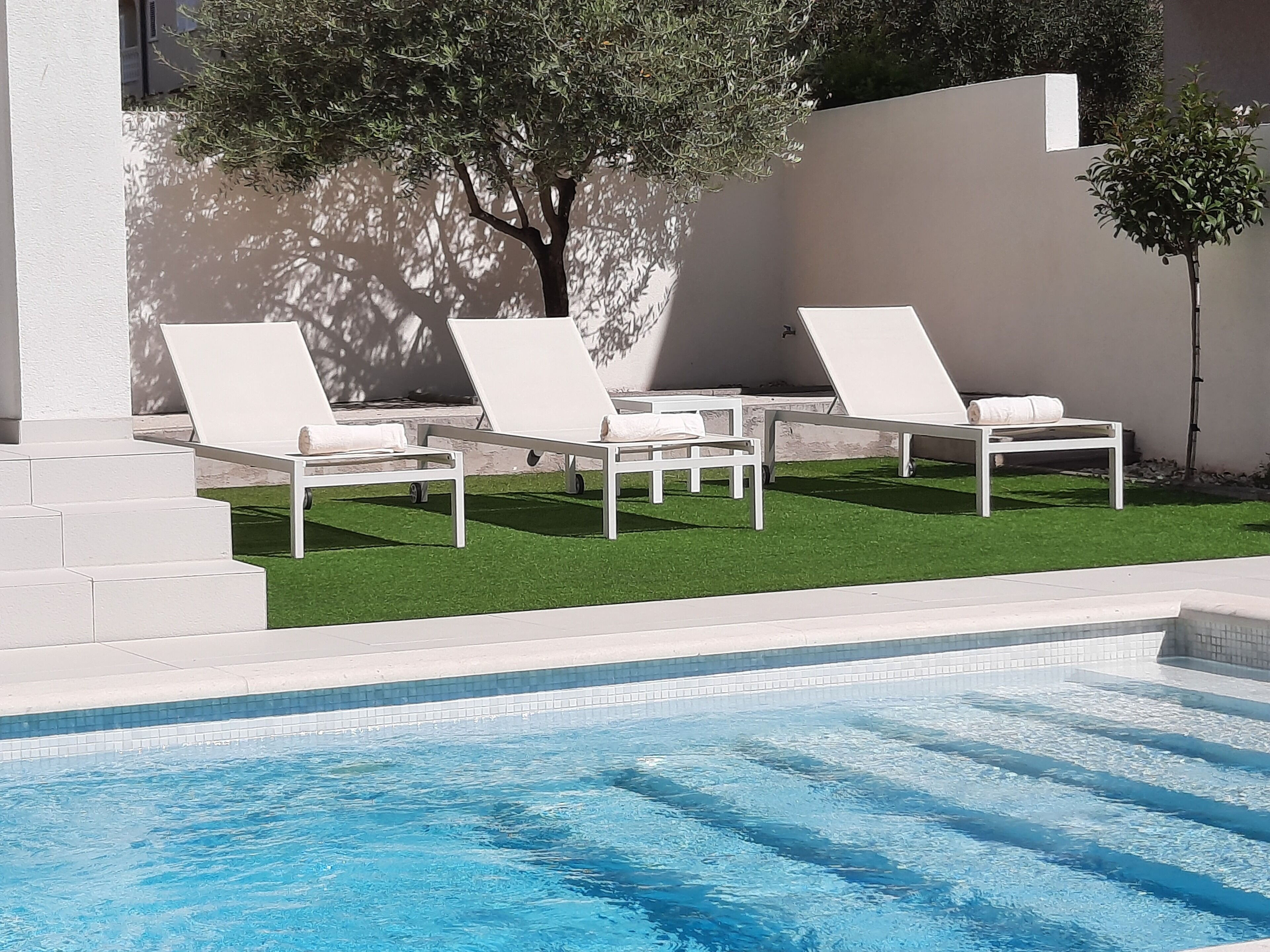Una piscina con sillones blancos y césped artificial.