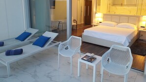Una habitación de hotel con una cama, un espacio de descanso con un banco y sillas, y una mesita con un libro.