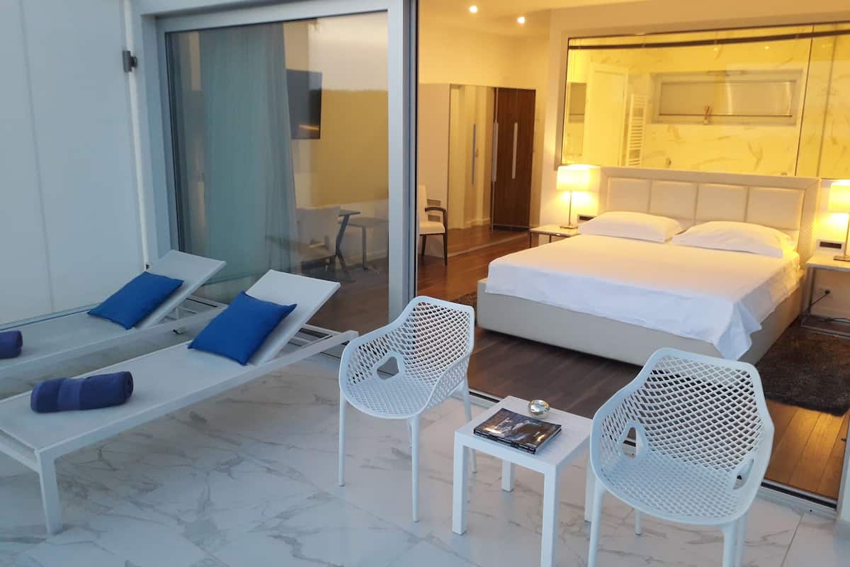 A hotel room with a bed, a sitting area with a bench and chairs, and a small table with a book.