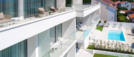 Un edificio moderno de varios pisos con piscina en la azotea, zona de estar al aire libre y un jardín cuidado.