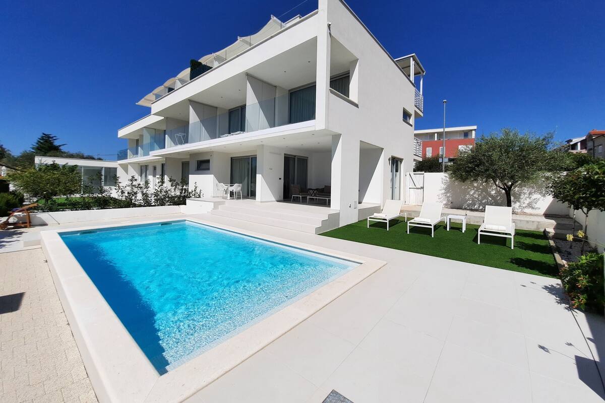 A modern two-story house with a swimming pool and outdoor seating.