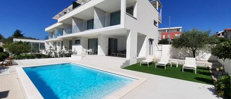 A modern two-story house with a swimming pool and outdoor seating.