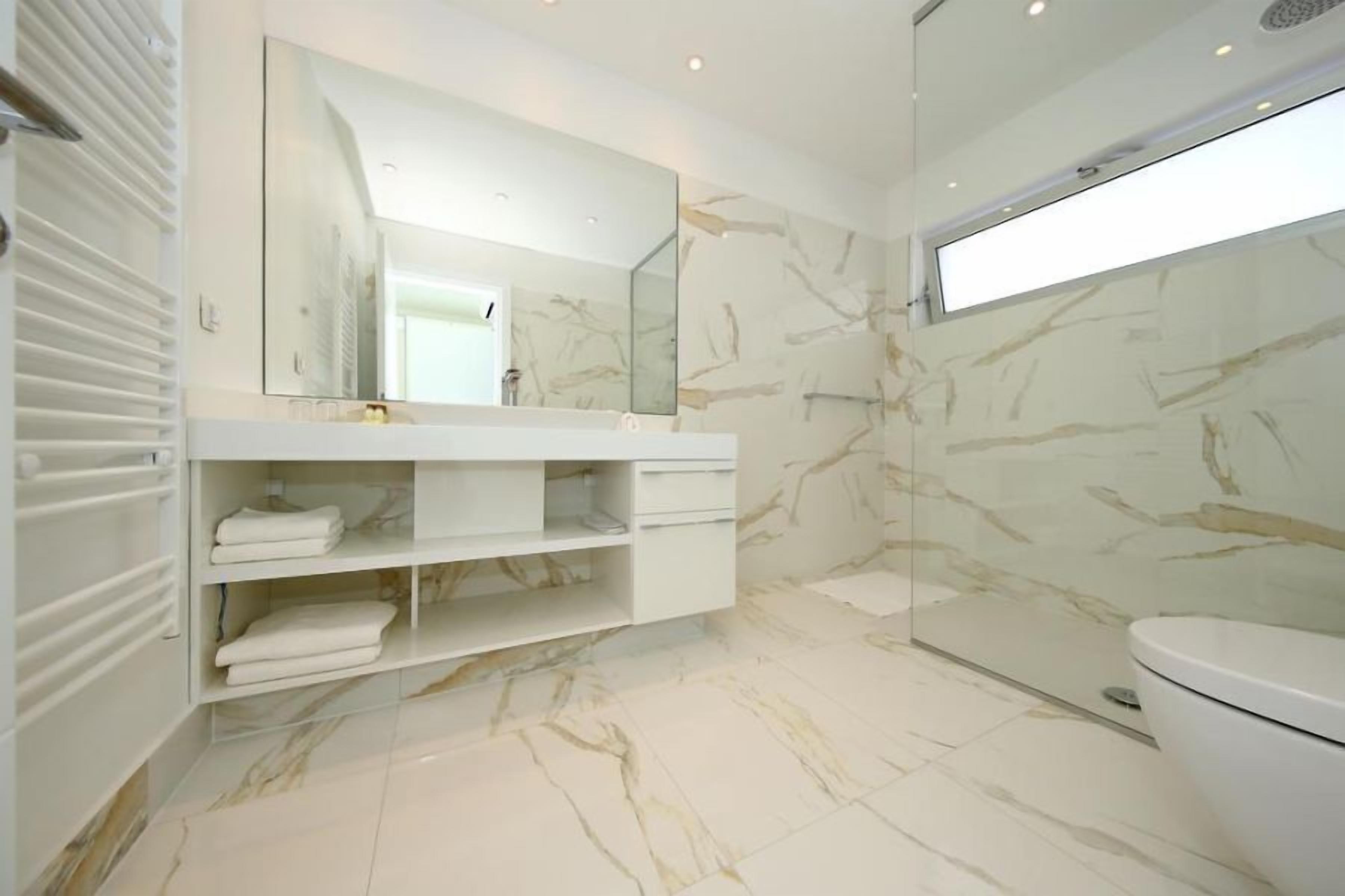 A modern bathroom with a marble floor, a large mirror, a white sink, and a toilet.