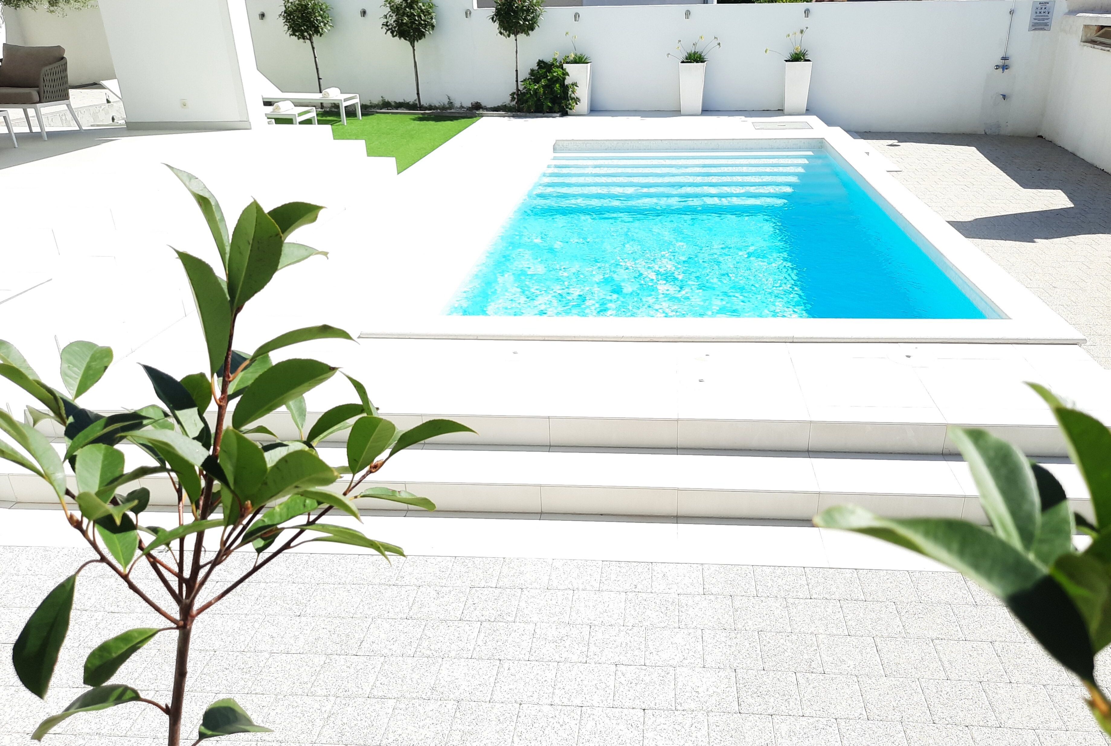 Uma piscina retangular com superfície de água azul cristalina, rodeada por um deck de azulejos brancos.