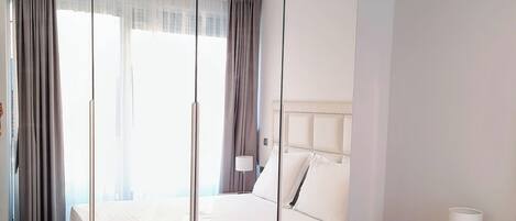 Une chambre d’hôtel moderne avec un grand lit, une table de chevet avec une lampe, une armoire et une fenêtre avec des rideaux.