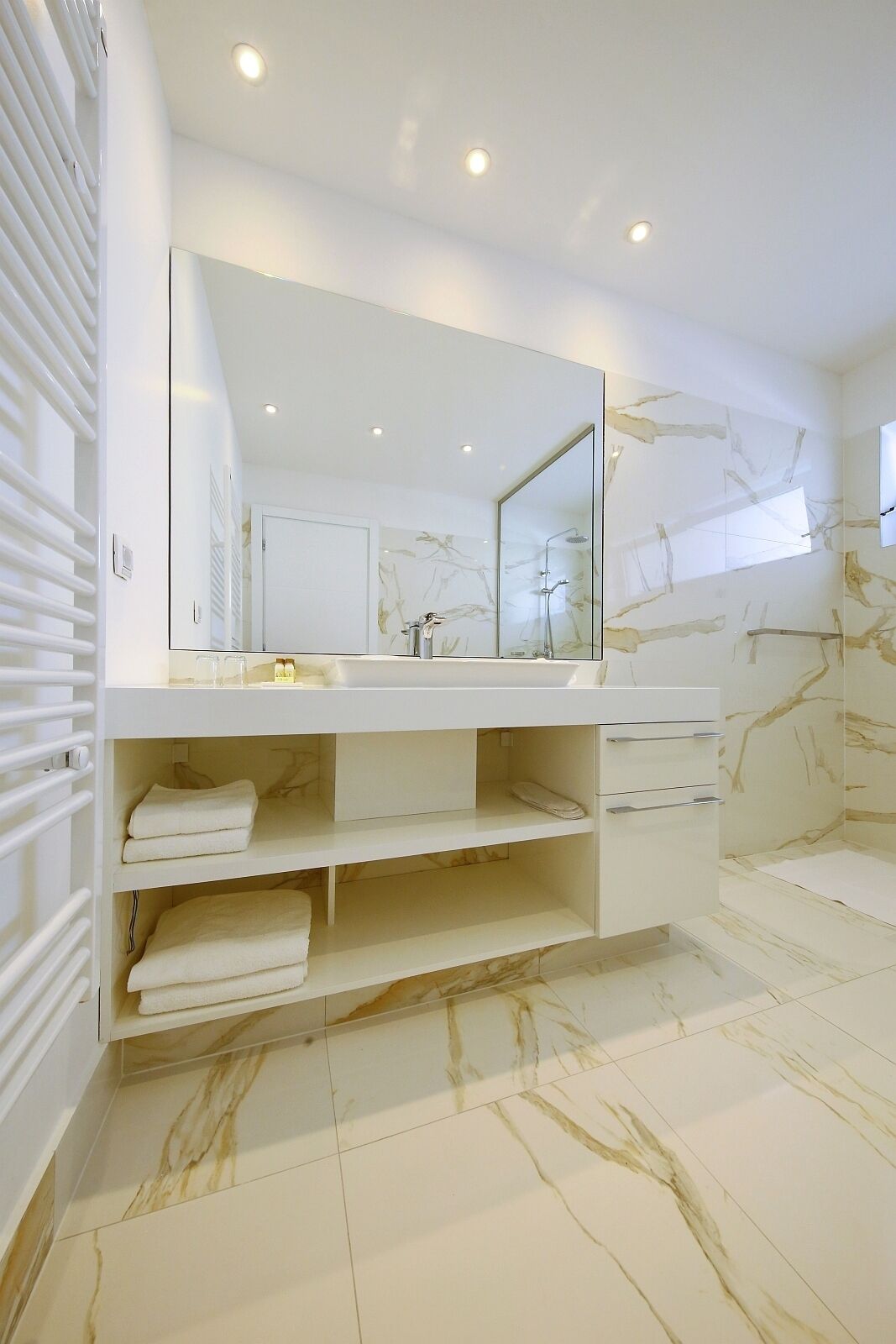 Un baño moderno con un espejo grande, estantes integrados y suelo de mármol.