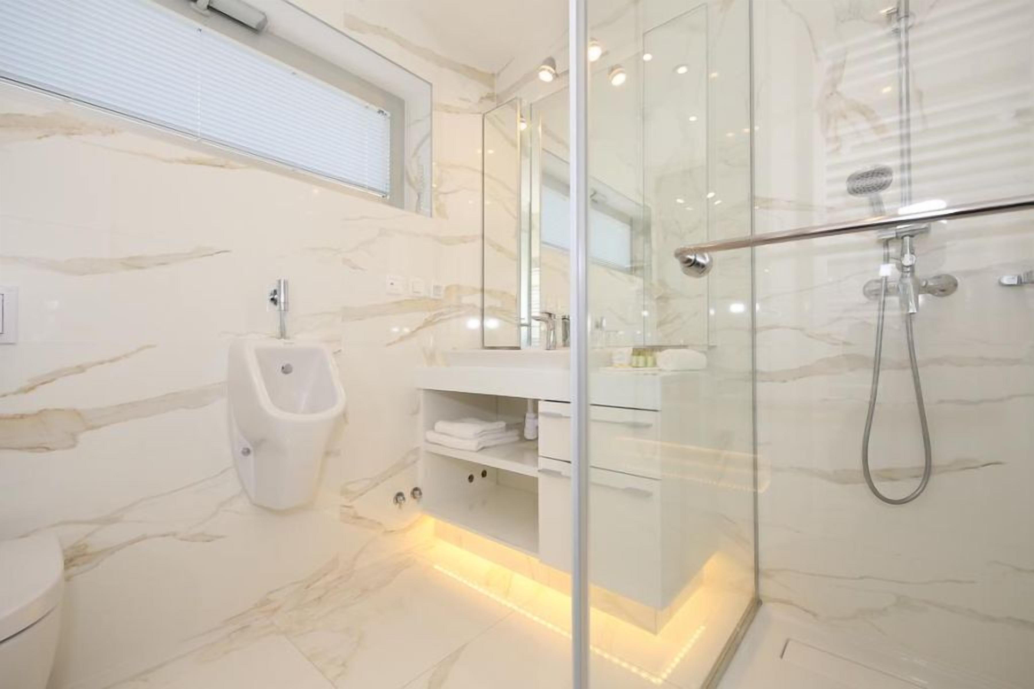A modern bathroom with a glass shower enclosure, marble flooring, and a white vanity with storage.