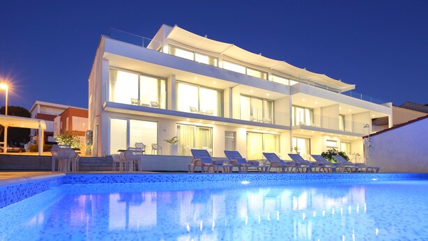 Un hotel moderno con piscina, sillones de descanso y una fachada bien iluminada al anochecer.