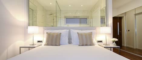 A modern hotel room with a large bed, two bedside lamps, and a large mirror above the bed.