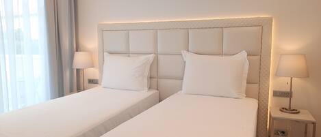 A hotel room with two single beds, a bedside table with a lamp, and a window with curtains.