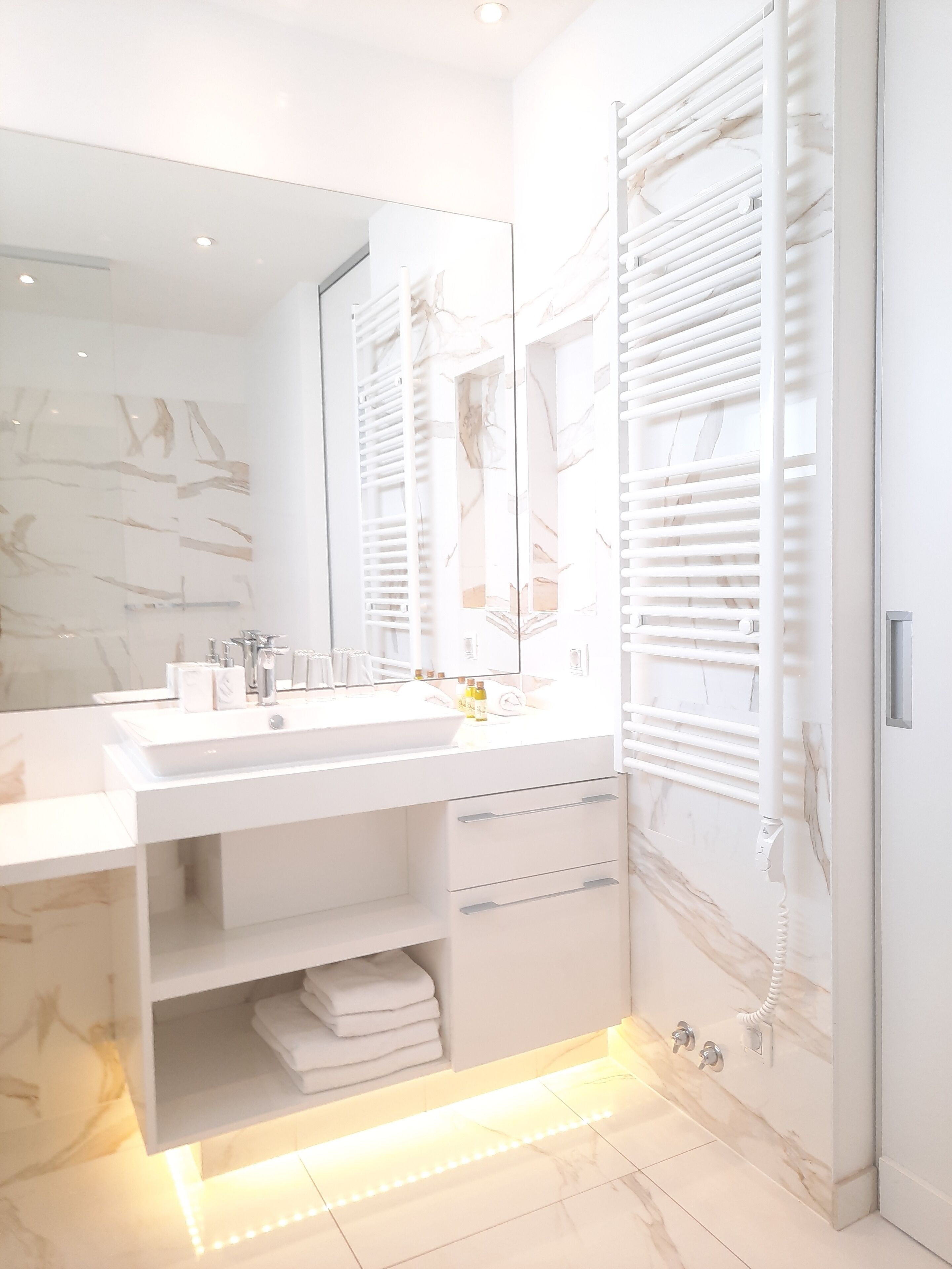 A modern bathroom with a large mirror, white vanity, and built-in towel rack.
