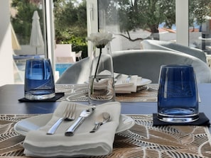 Una mesa dispuesta con vasos azules, una servilleta blanca, cubiertos y un jarrón con una flor blanca.