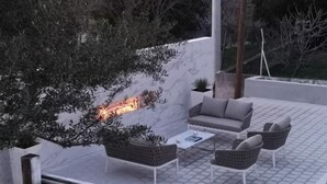 Un patio al aire libre con un sofá, sillas y una mesa baja. Se observa una pared con una planta y una mesita.