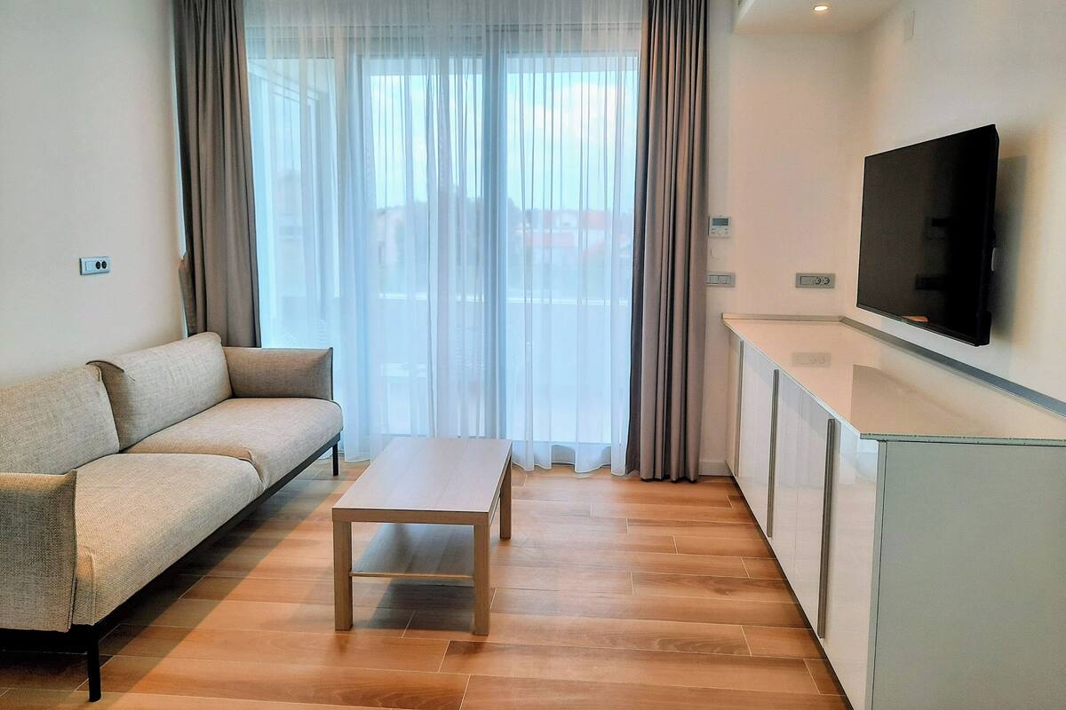 A modern living room with a sofa, a coffee table, and a flat-screen TV mounted on the wall.